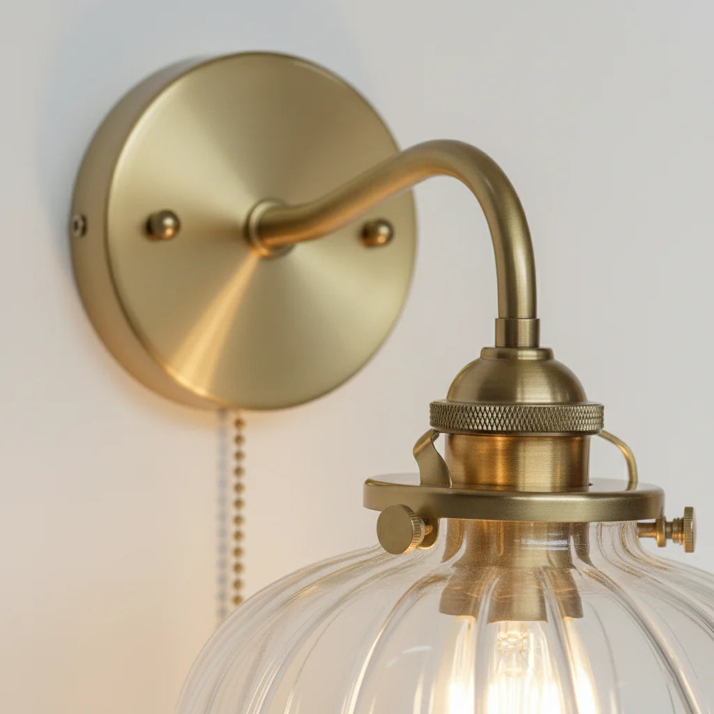 Närbild på glaskupa och guldfärgad metallarm på vägglampa
