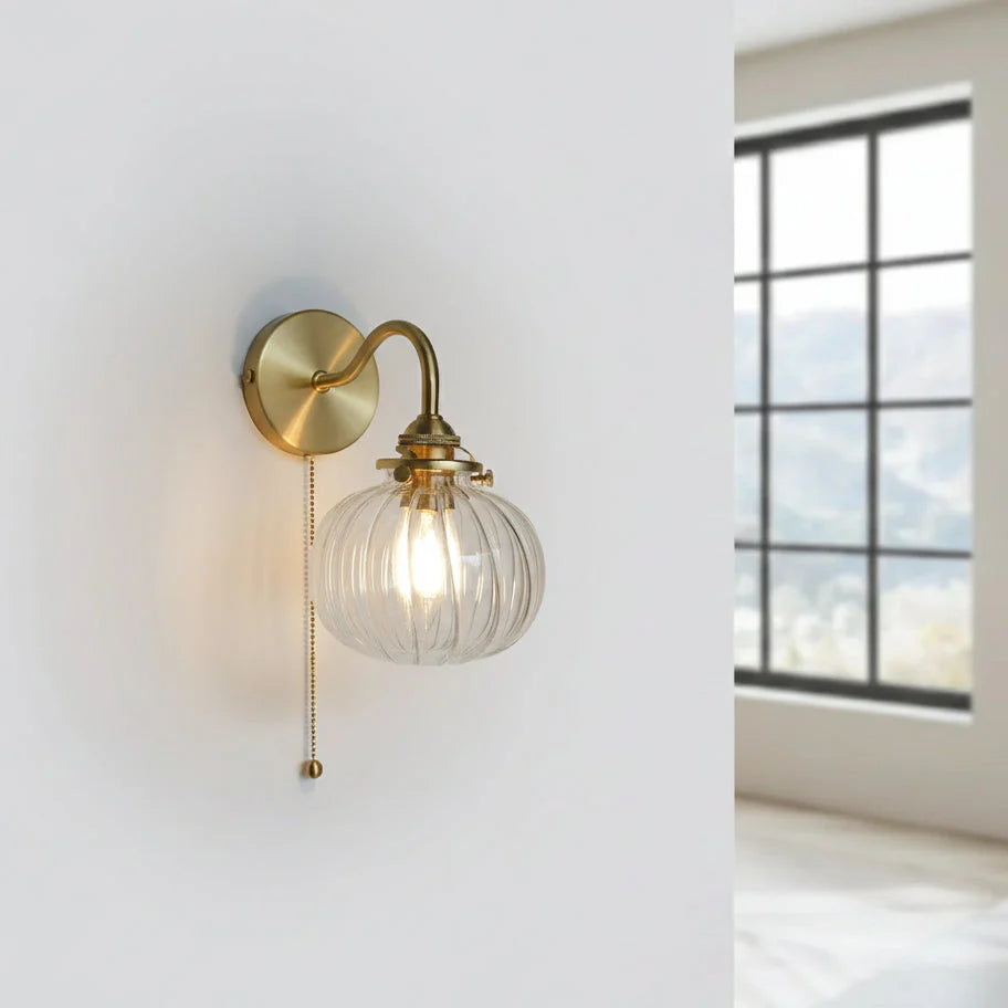 Vägglampa i glas och guldfärgad metall sedd framifrån